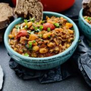 Baked beans recipe with ground beef served in a green serving bowl with a slice of bread tucked in closeup.