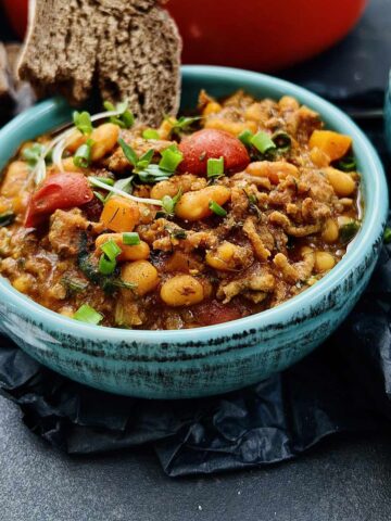 Baked beans recipe with ground beef served in a green serving bowl with a slice of bread tucked in closeup.