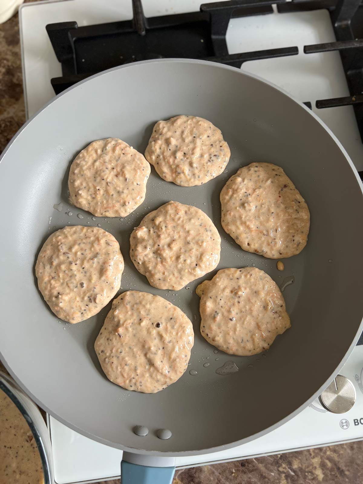 Carrot, apple and butternut squash pancakes batter in a grey pan being cooked