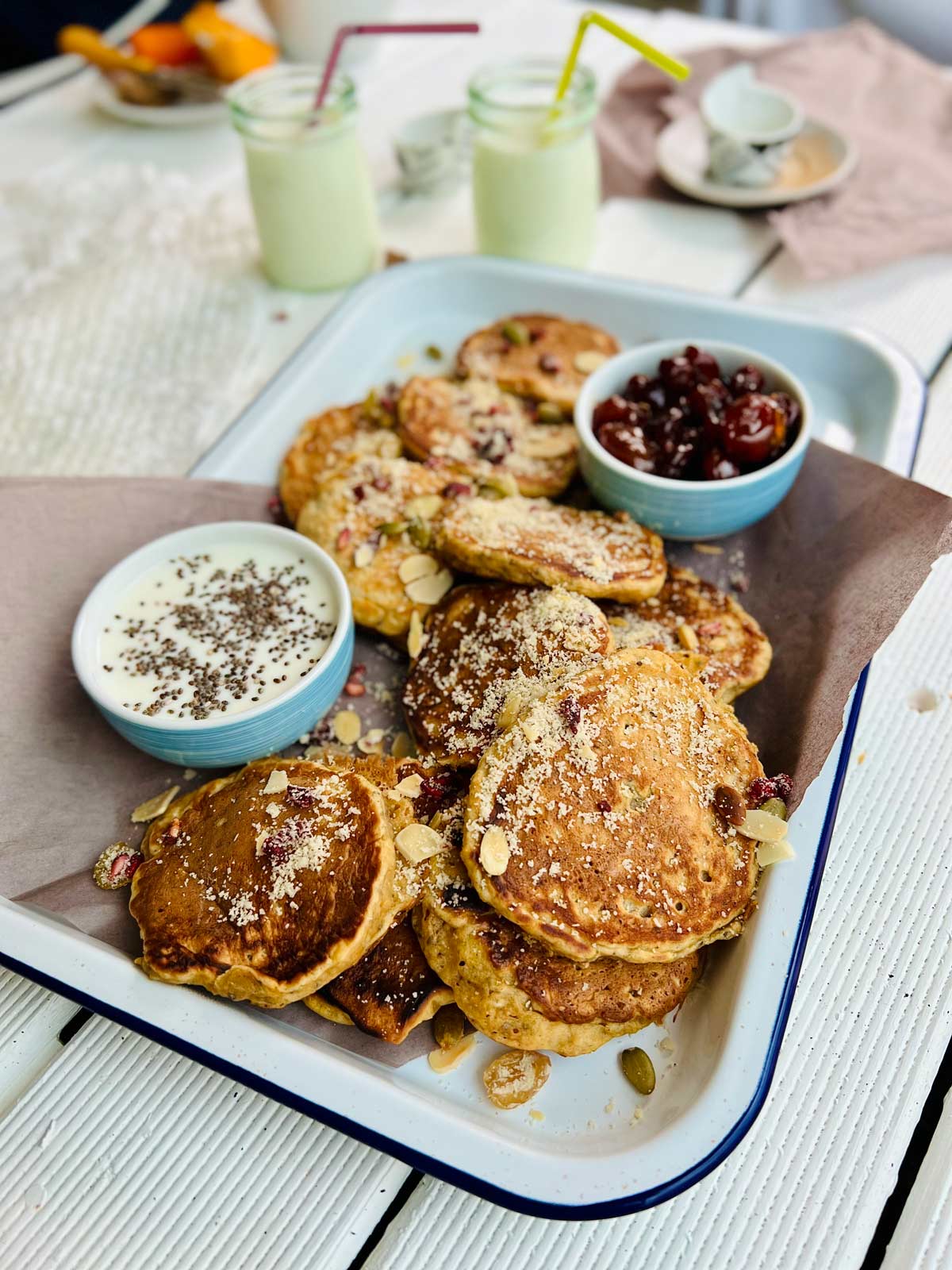 Butternut squash pancakes on white tray with the blue dream with two serving dishes, one with jam, one with yoghurt and chia seeds sprinkled over