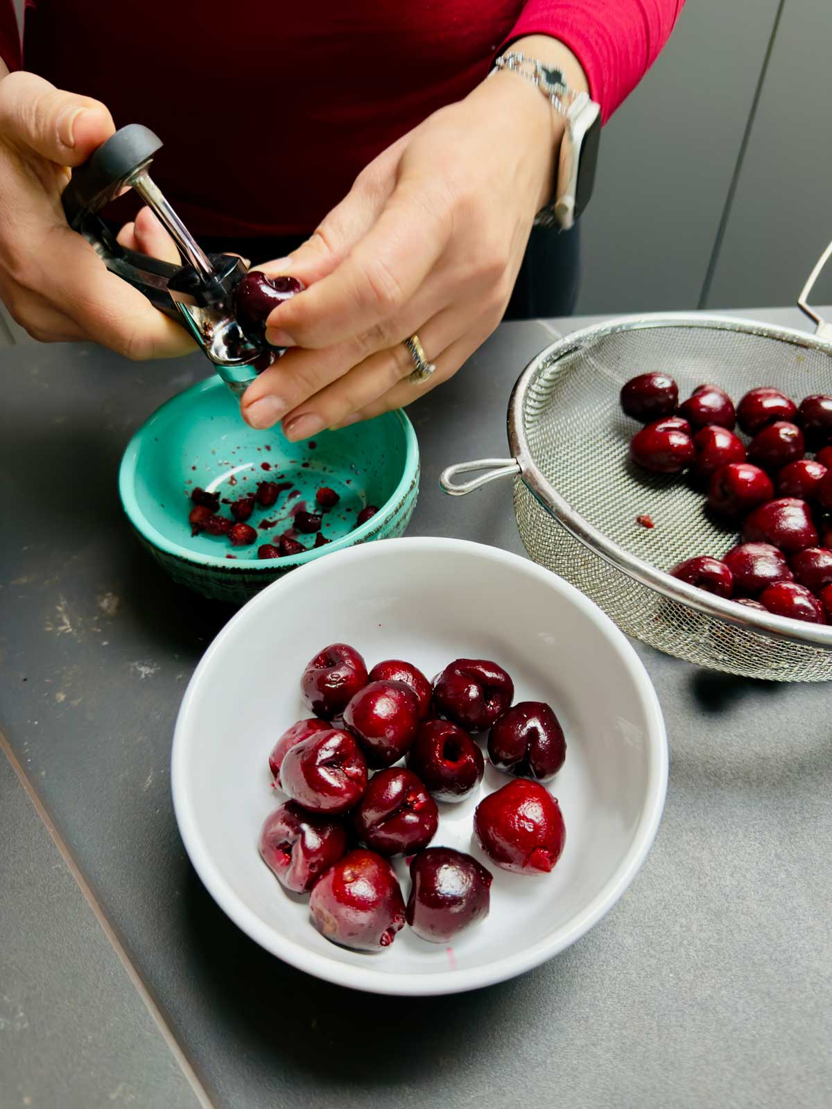 Cherries being pitted and put in a white ceramic bowl.