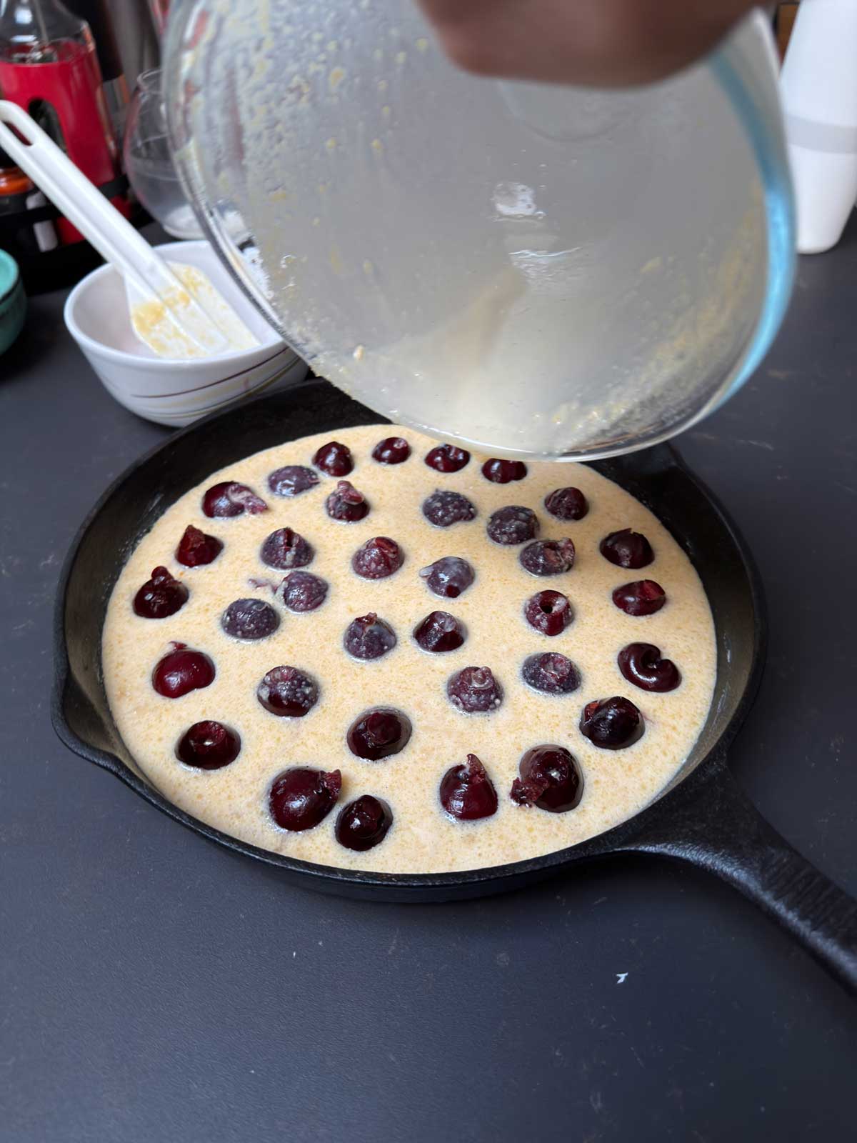 Clafoutis Batter added to the cherries in a cast iron skillet.