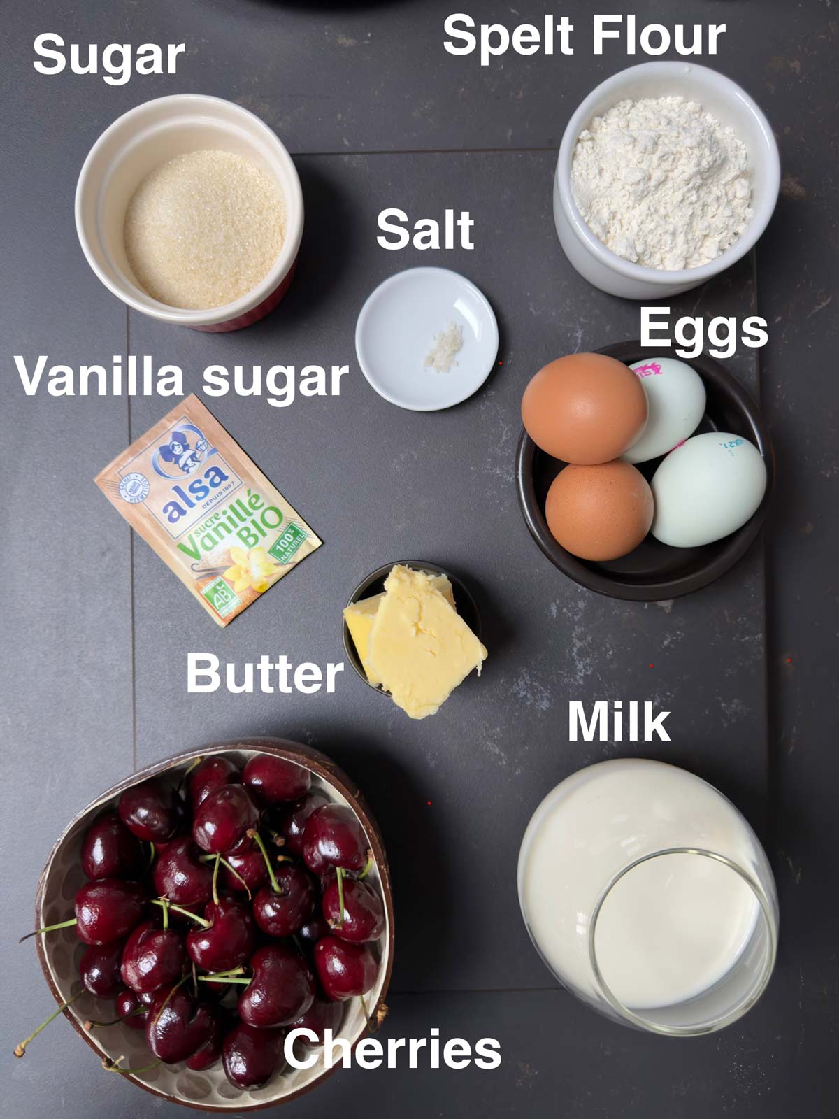 Ingredients needed for clafoutis aux cerises, spelt flour, sugar, salt, eggs, vanilla, butter, milk, cherries.