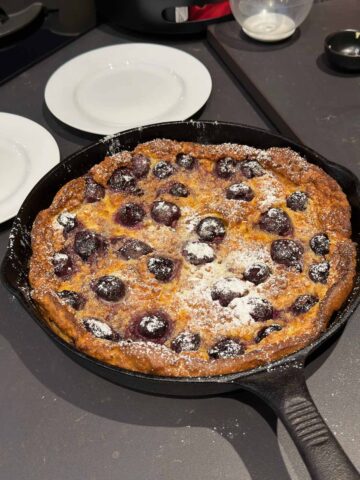 Clafoutis dessert with icing sugar powdered on top in a cast iron skillet.
