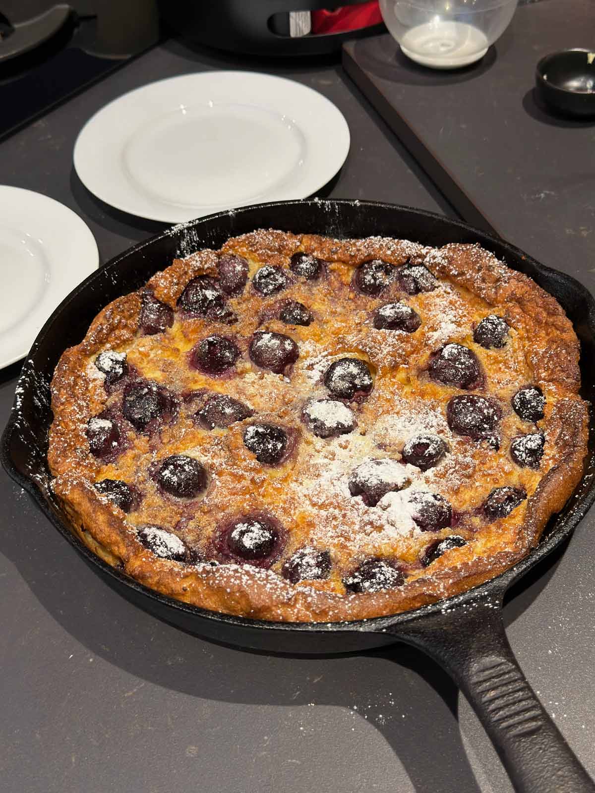 Clafoutis dessert with icing sugar powdered on top in a cast iron skillet.