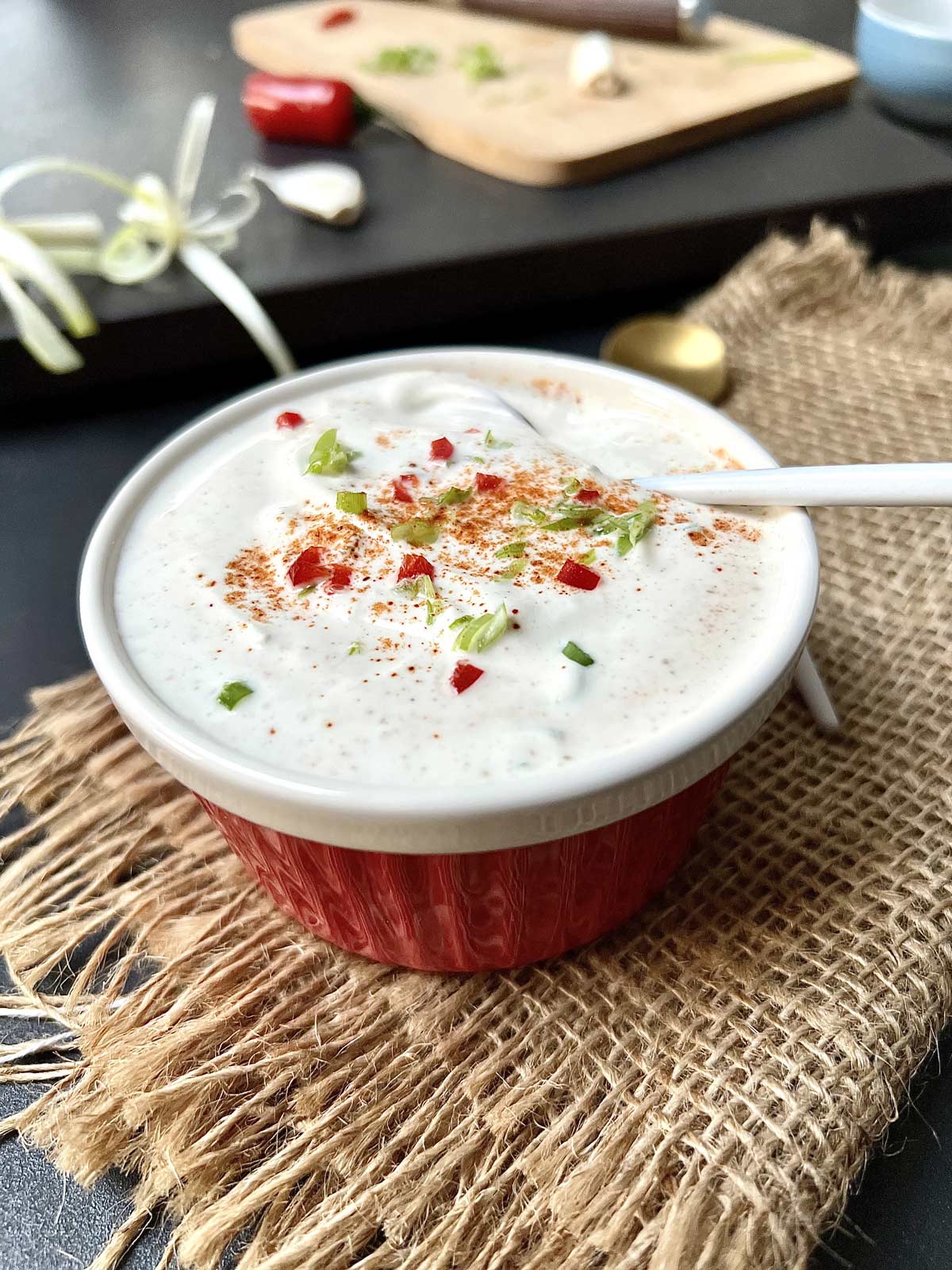 Close up of creamy sour cream sauce in a ceramic bowl with a teaspoon tucked in.