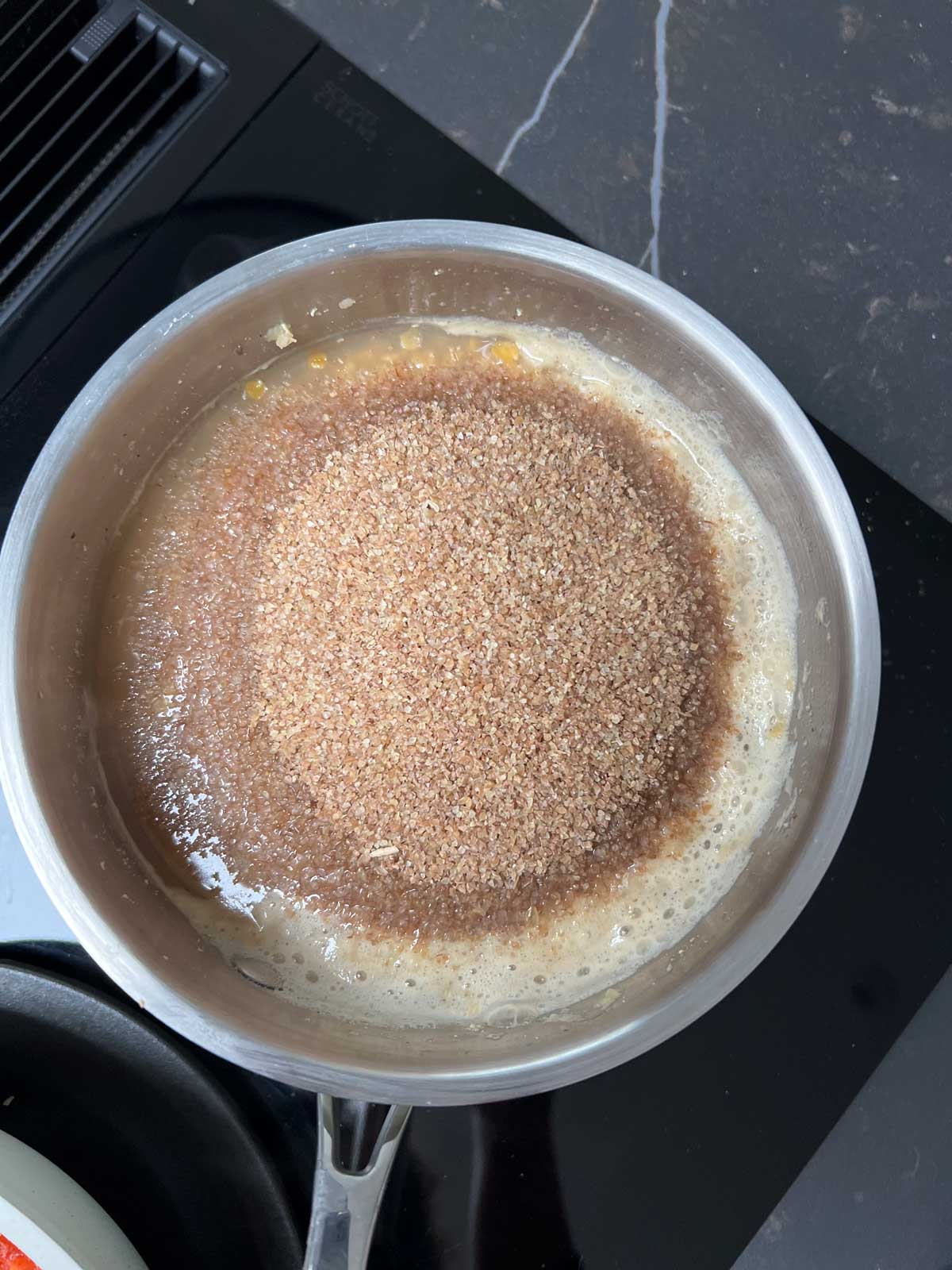 Cooked lentils with bulgur added in a pan on a black ceramic stove.