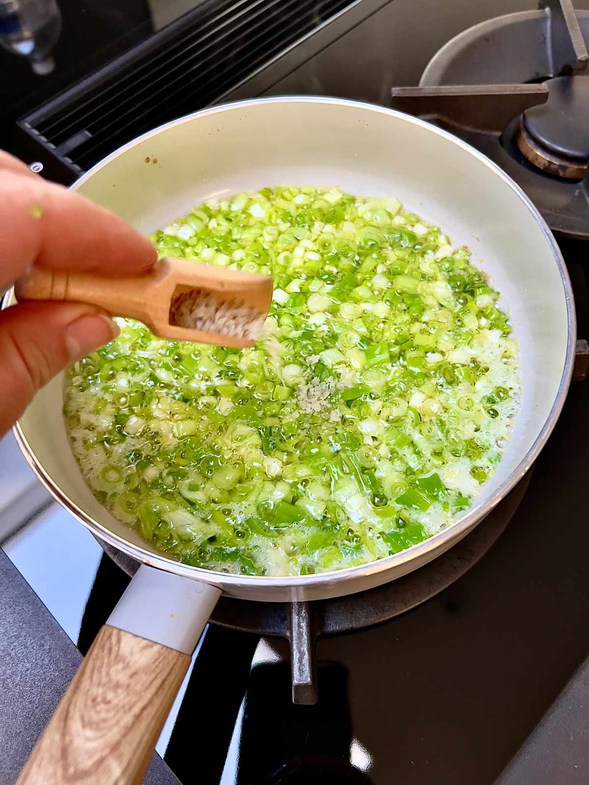 Cooking scallions in a pan, salt being added.