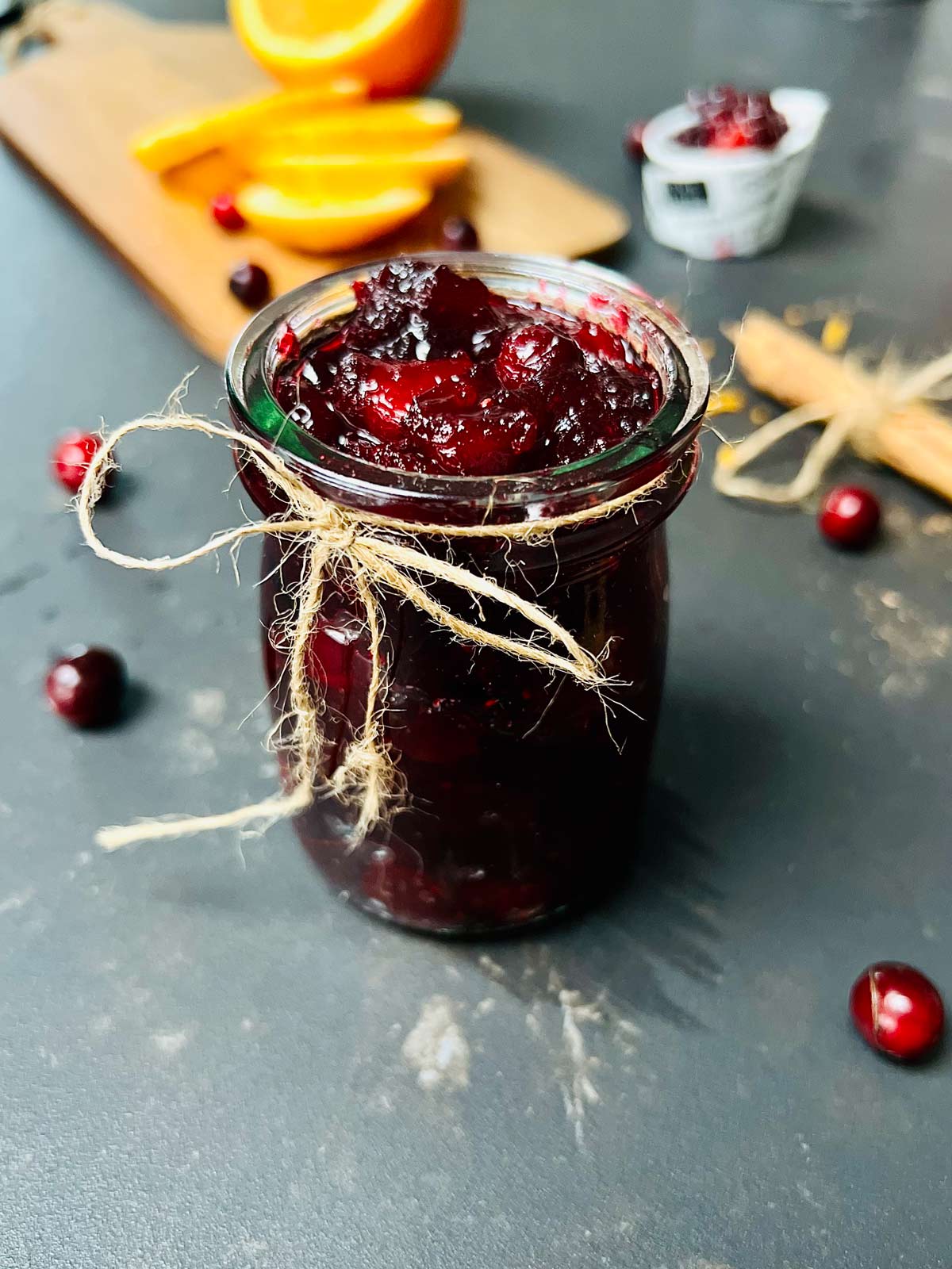 Cranberry preserve in a jar with a little rope tied in a bow around the neck of the jar.