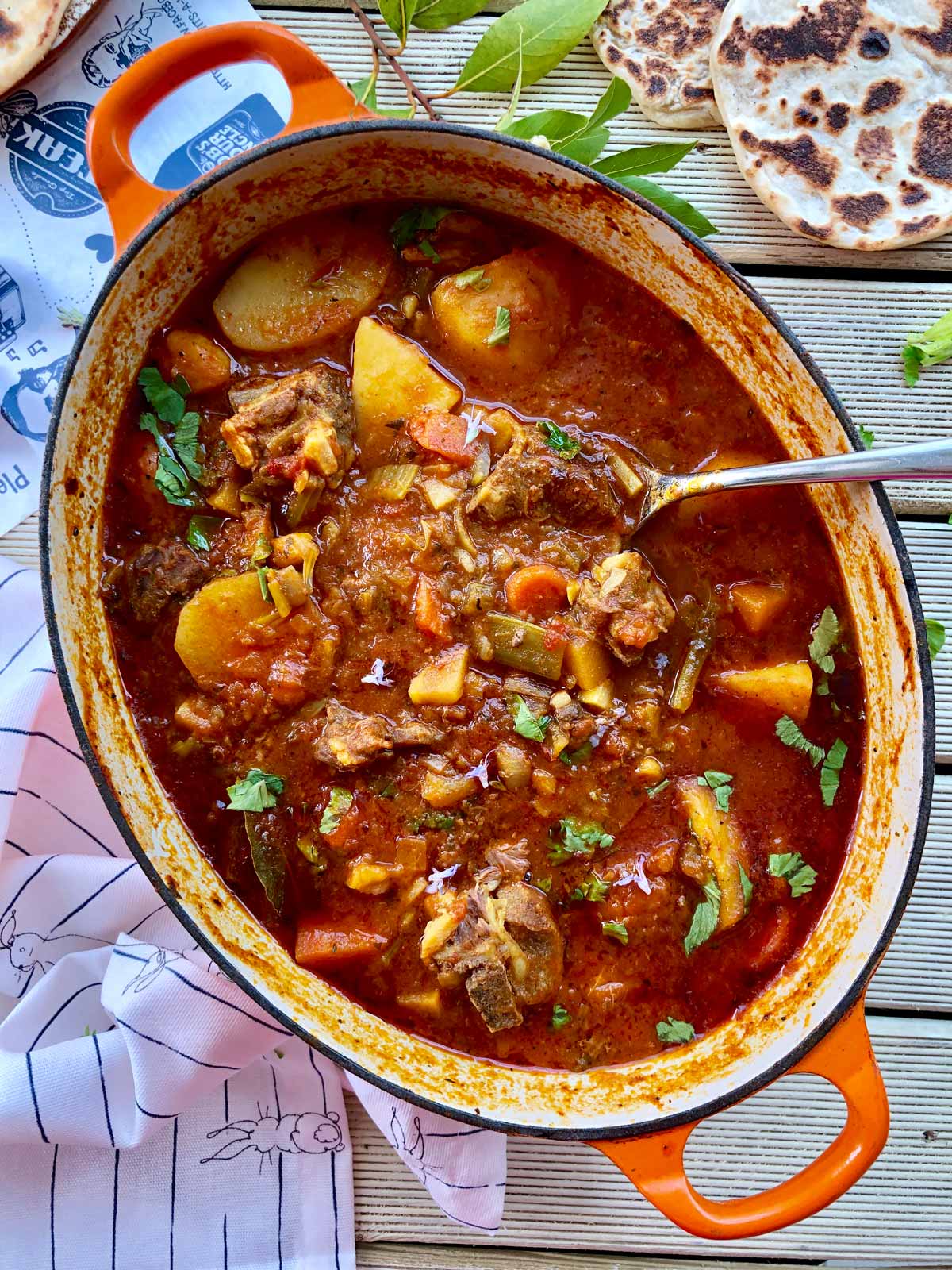 Birds view of beef casserole in an oval orange cast iron dish with flatbread top right