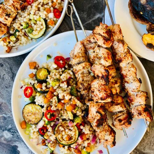 4 Chicken kebabs on a white plate with mixed vegetable couscous.