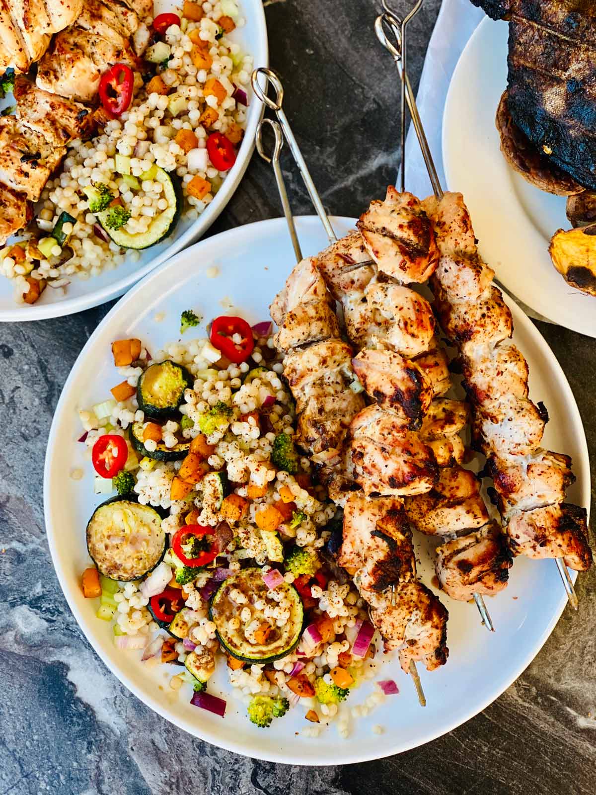 4 Chicken kebabs on a white plate with mixed vegetable couscous