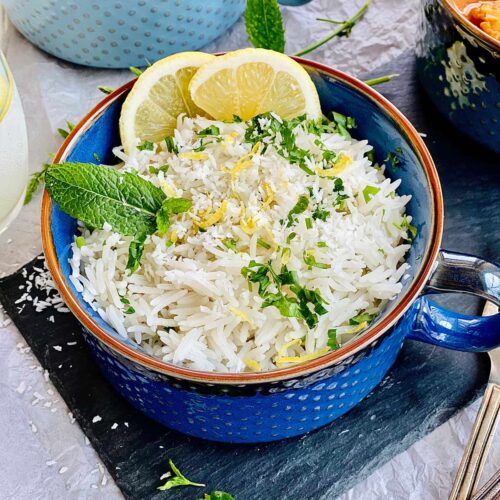 Instant pot coconut rice in a blue serving bowl garnished with lemon, lemon rind and mint