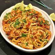 Easy prawn and chorizo pasta in an oval serving plate with a few lemon slices and a sprinkle of chopped parsley.