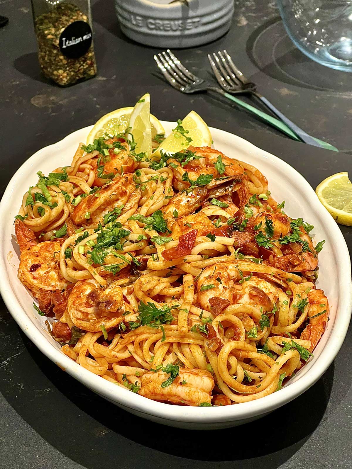Easy prawn and chorizo pasta in an oval serving plate with a few lemon slices and a sprinkle of chopped parsley.