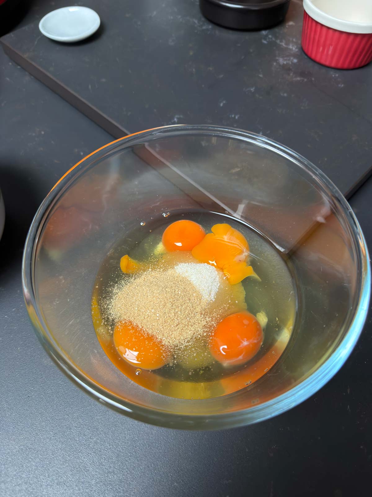 Eggs, sugar, vanilla added to a clear glass bowl.