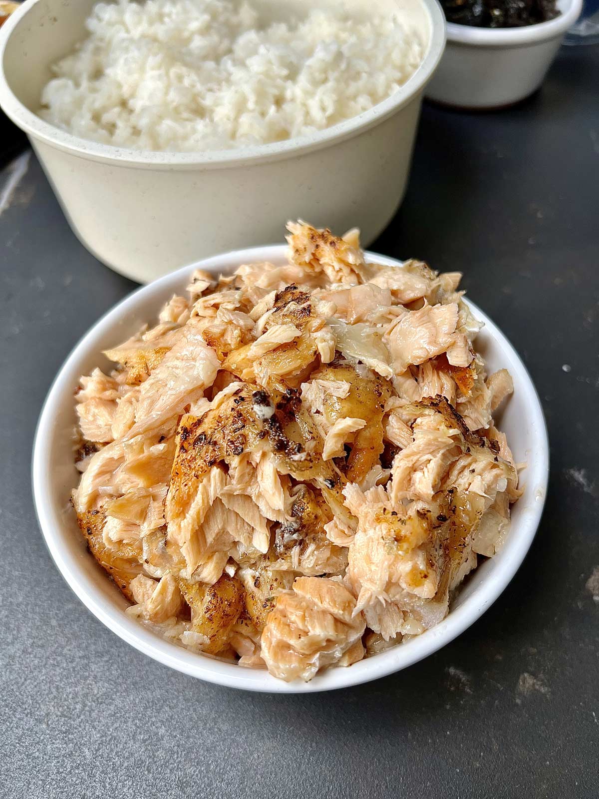 Flaked baked salmon in a white bowl and a rice bowl at the top.