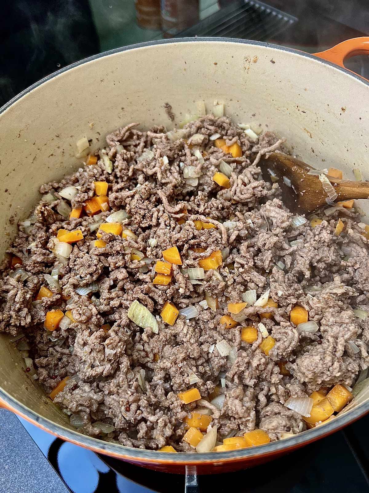 Half cooked ground beef with carrots, onions and spices with a wooden spoon tucked in.