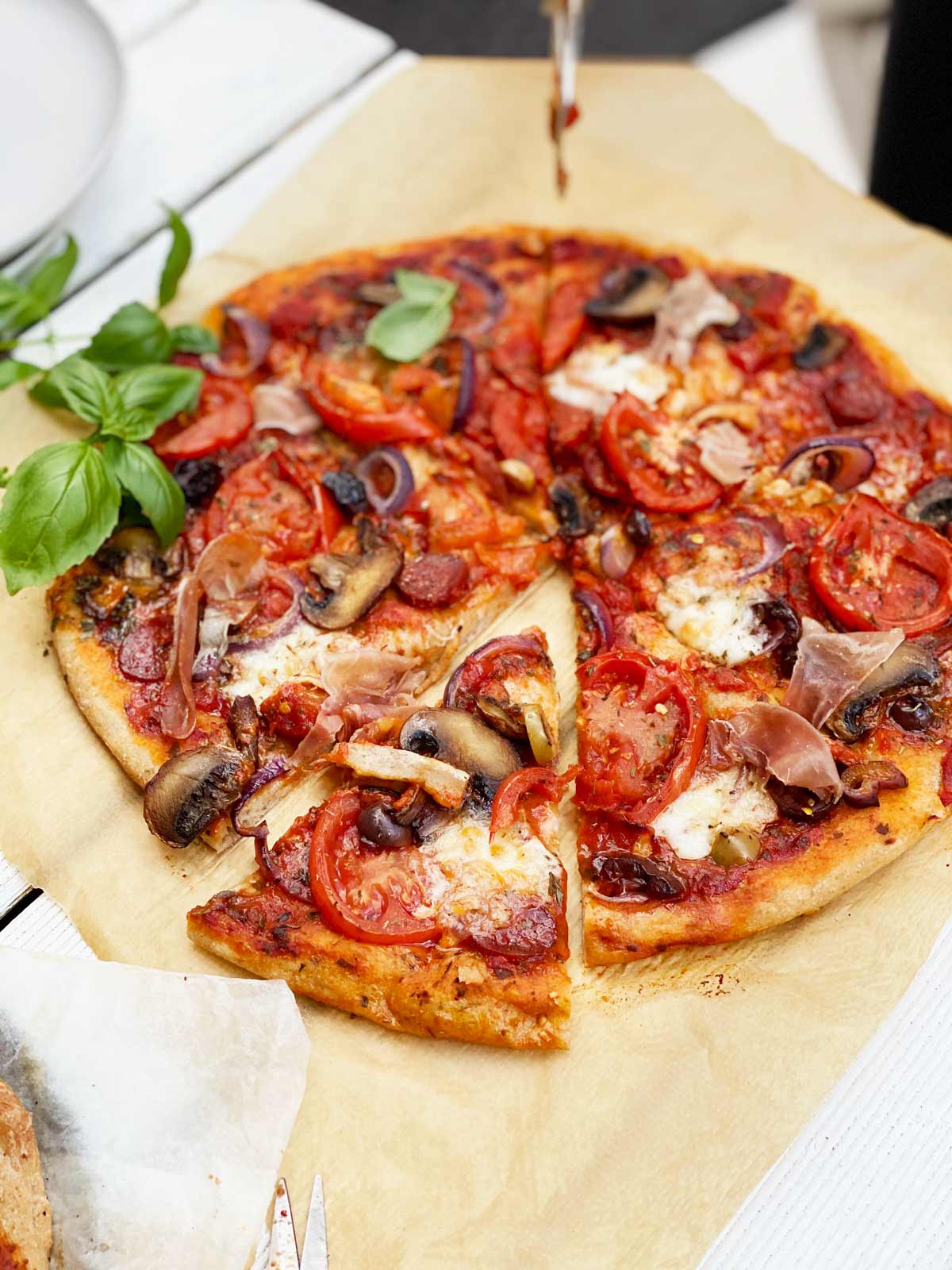 Homemade pizza in the centre with 2 sprigs of basil on the left over on brown parchment paper