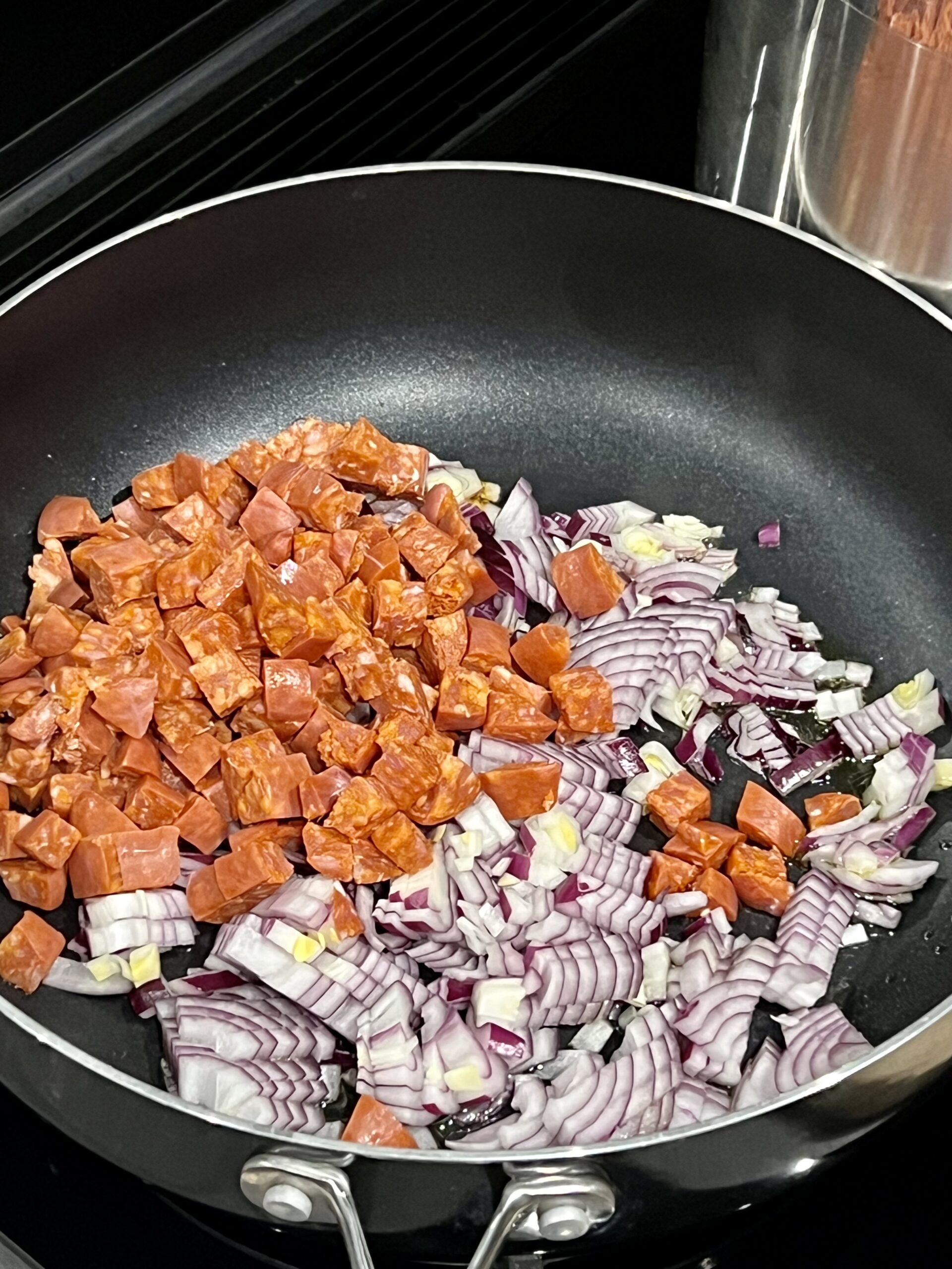 Chopped chorizo sausage, red onion and garlic in a pan being cooked.