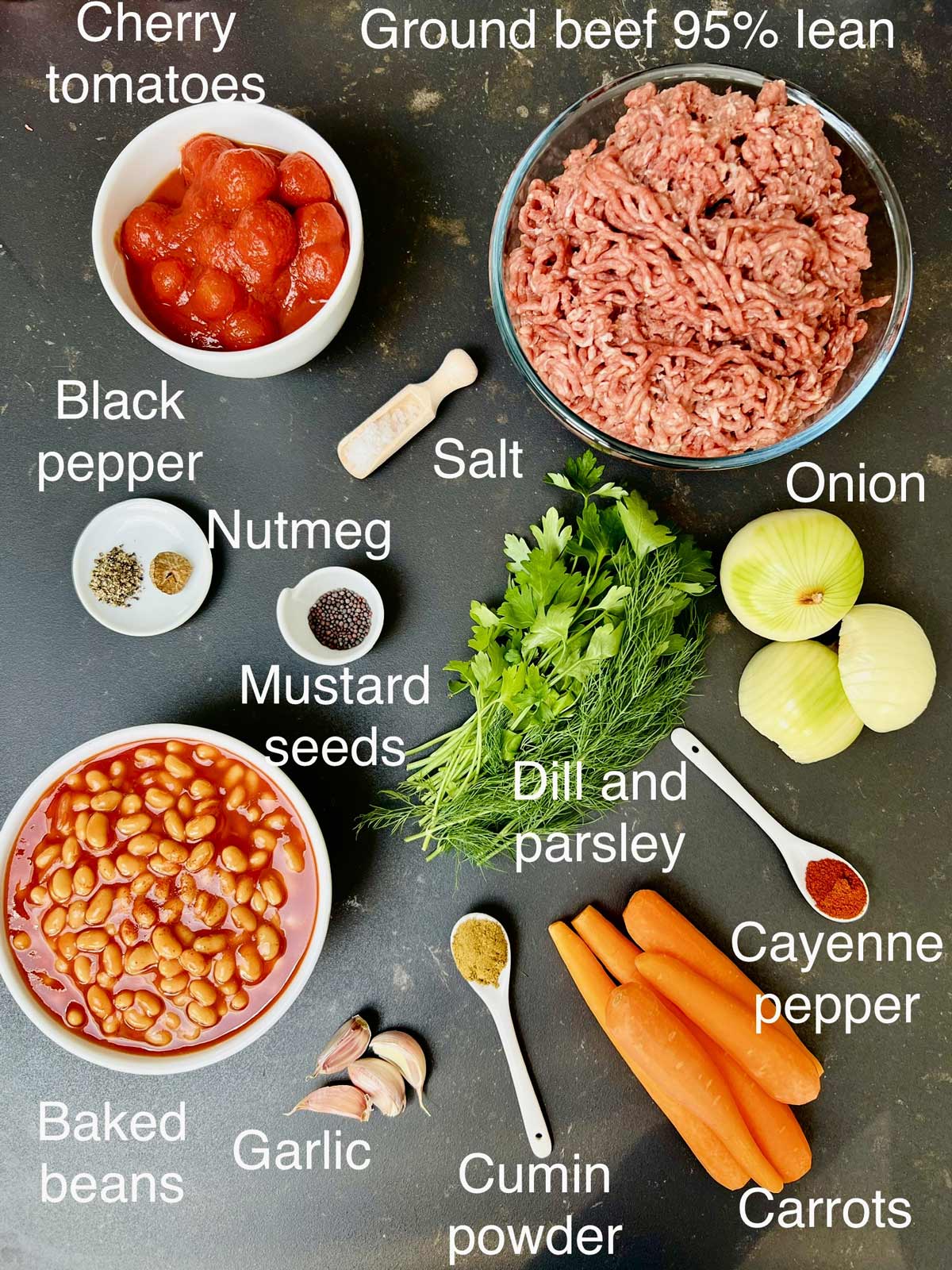 Ingredients (ground beef, canned cherry tomatoes, spices, herbs, baked beans, carrots and onion) needed for baked beans with ground beef.