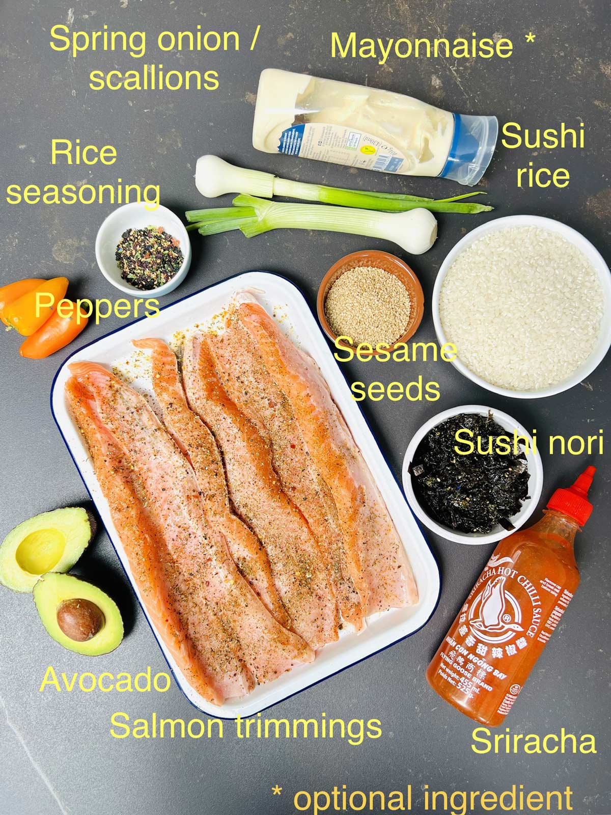 Ingredients needed for sushi bake (rice, spring, onion/scallions, rice, seasoning, peppers, sesame seeds, sushi nori, Sriracha sauce, avocado, salmon).