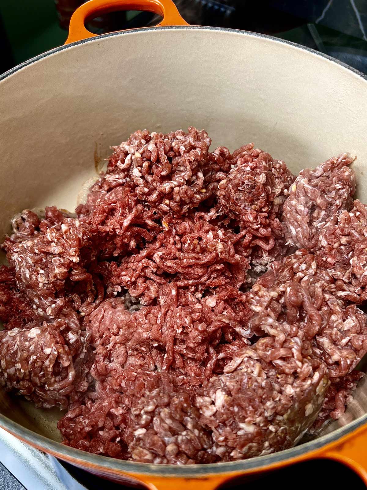 Lean Ground beef cooking in a Le Creuset orange pot.