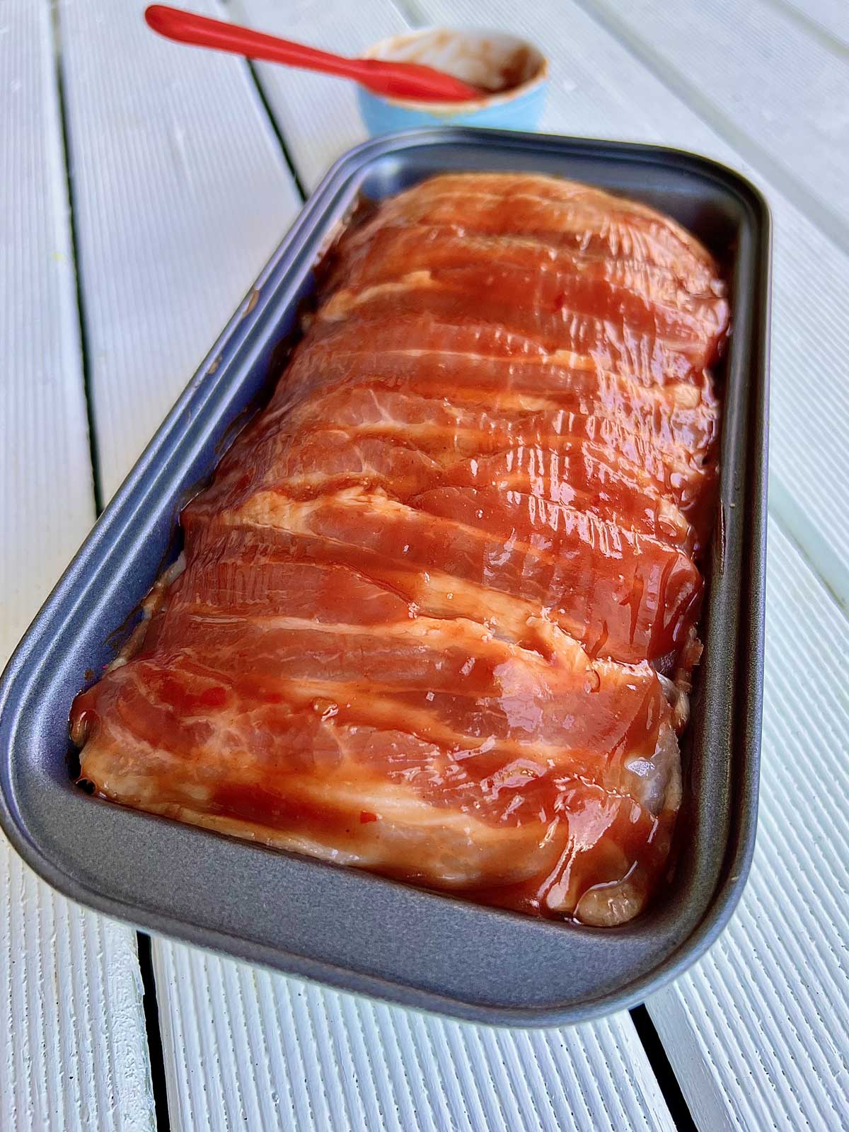 Meatloaf wrapped with bacon and brushed with homemade ketchup in a metallic tin ready to be cooked.