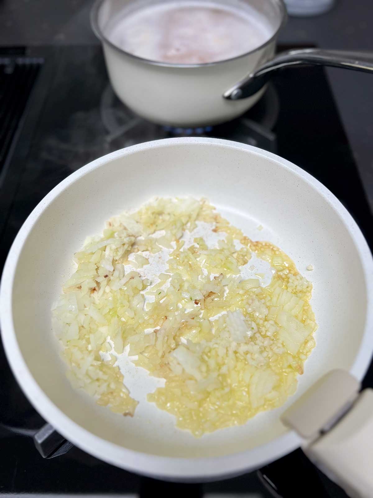 Onion sauteing in olive oil in a white frying pan.