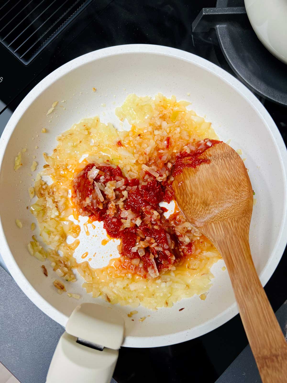 Onion, tomato and pepper paste mix cooking in a white pan with wooden spatula in.