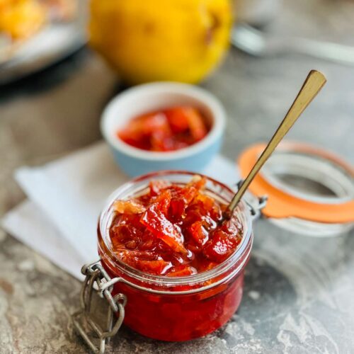 Quince jam in a preserve jar with the lid opened on the right and a teaspoon tucked all in