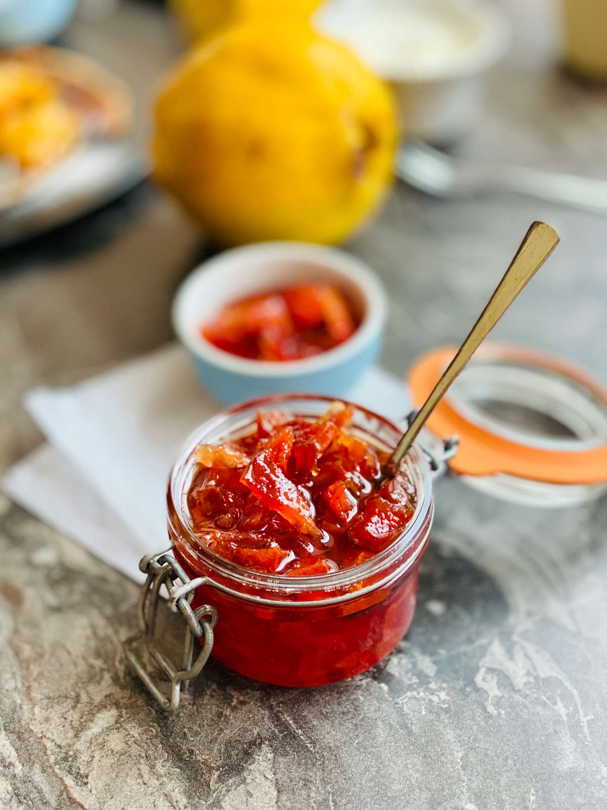 Quince jam in a preserve jar with the lid opened on the right and a teaspoon tucked all in