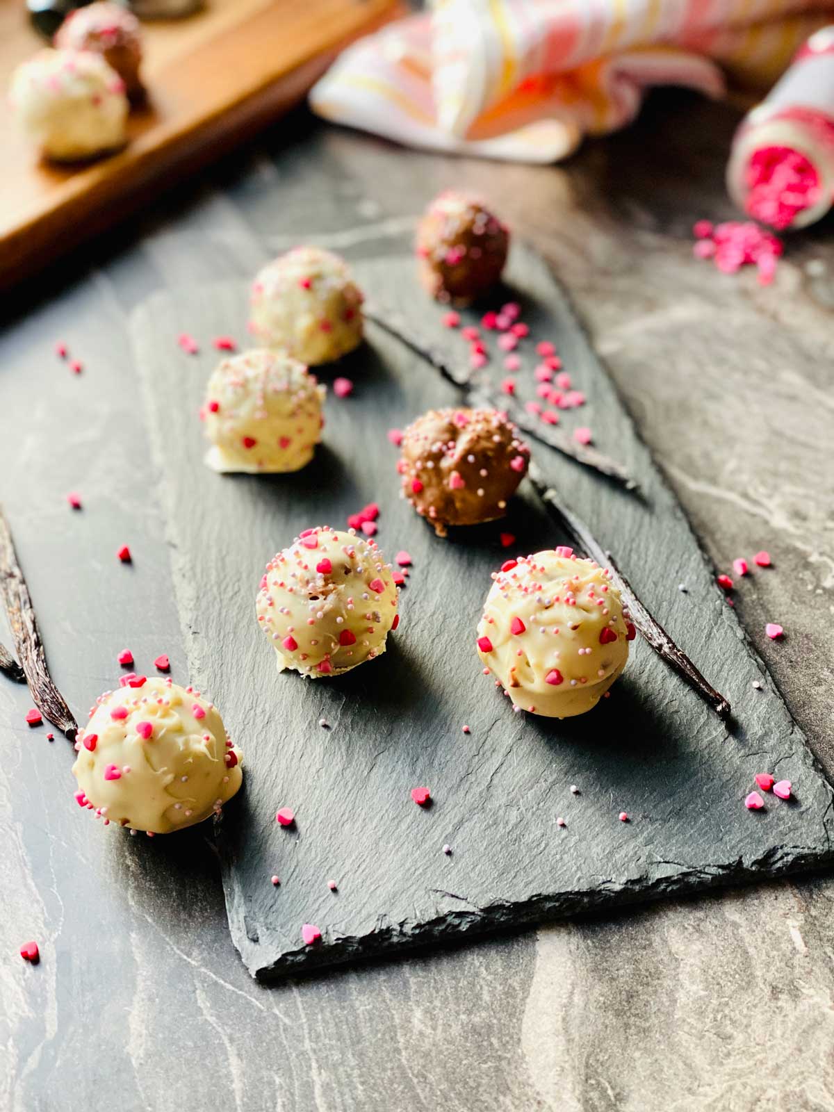 milk and chocholate cake pops on a black slate with two vanilla pods and scattered little pink sugar hearts