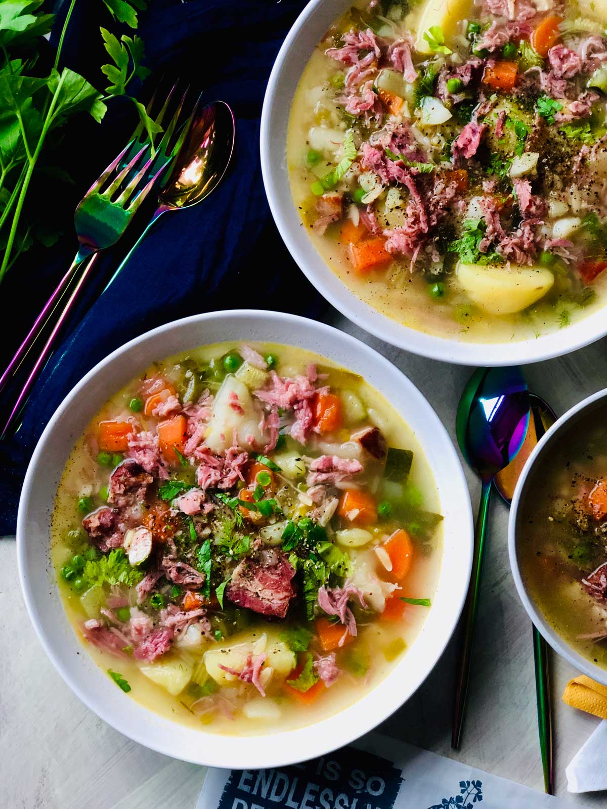 Potato soup with ham hock and petit pois seen from above in two white ceramic plates.