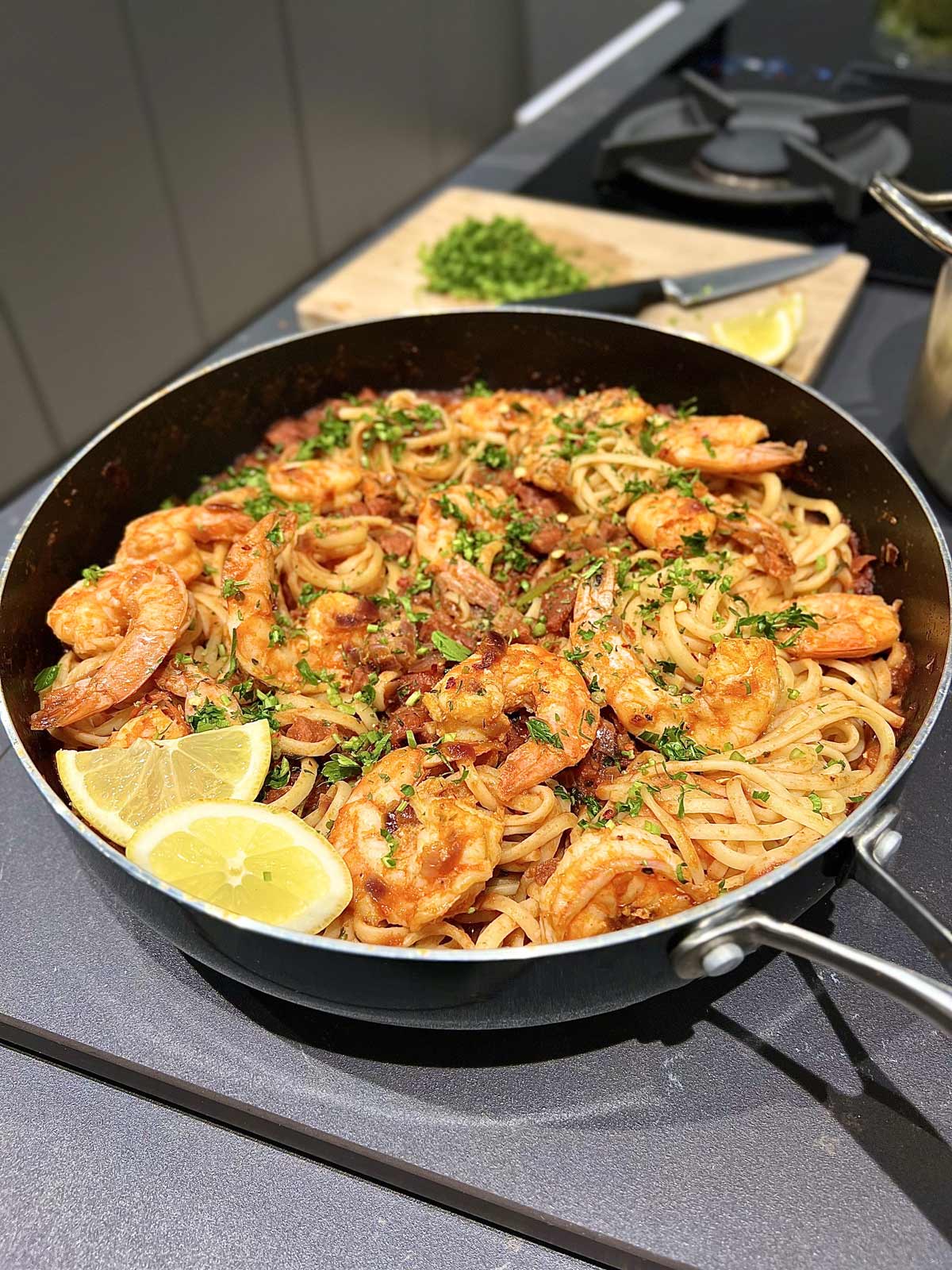 Shrimp and chorizo sausage pasta dish with two slices of lemon, in a black pan, ready to be served.