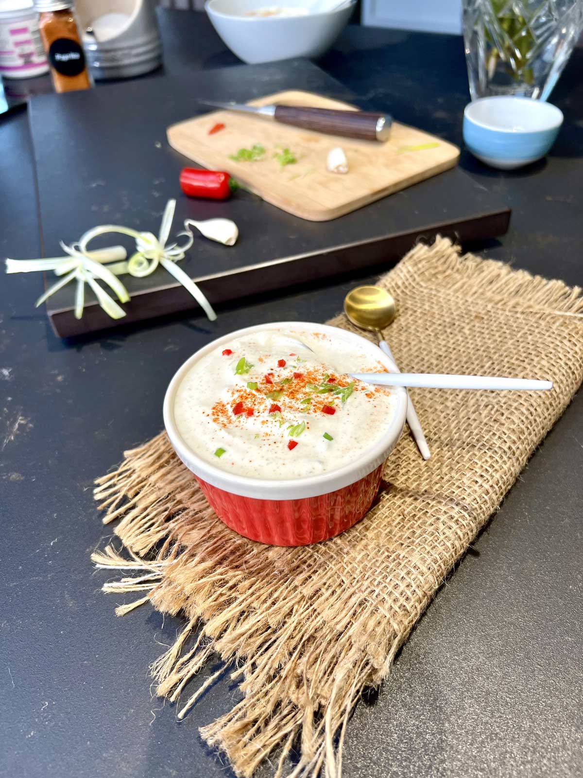 Silky sour cream sauce in a ceramic pot over a piece of jute on a black worktop.