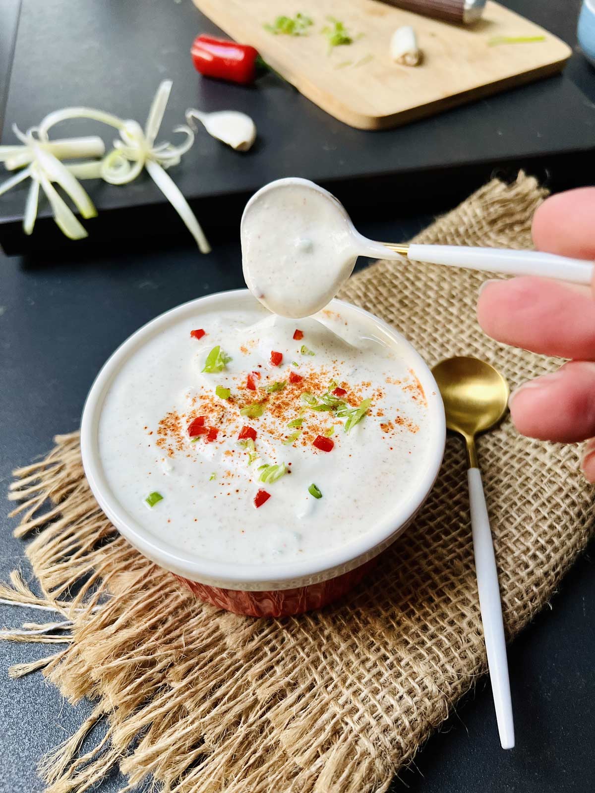 Sour cream sauce in red ceramic serving bowl with scallions, red pepper, and a dash of Cayenne pepper sprinkled over.