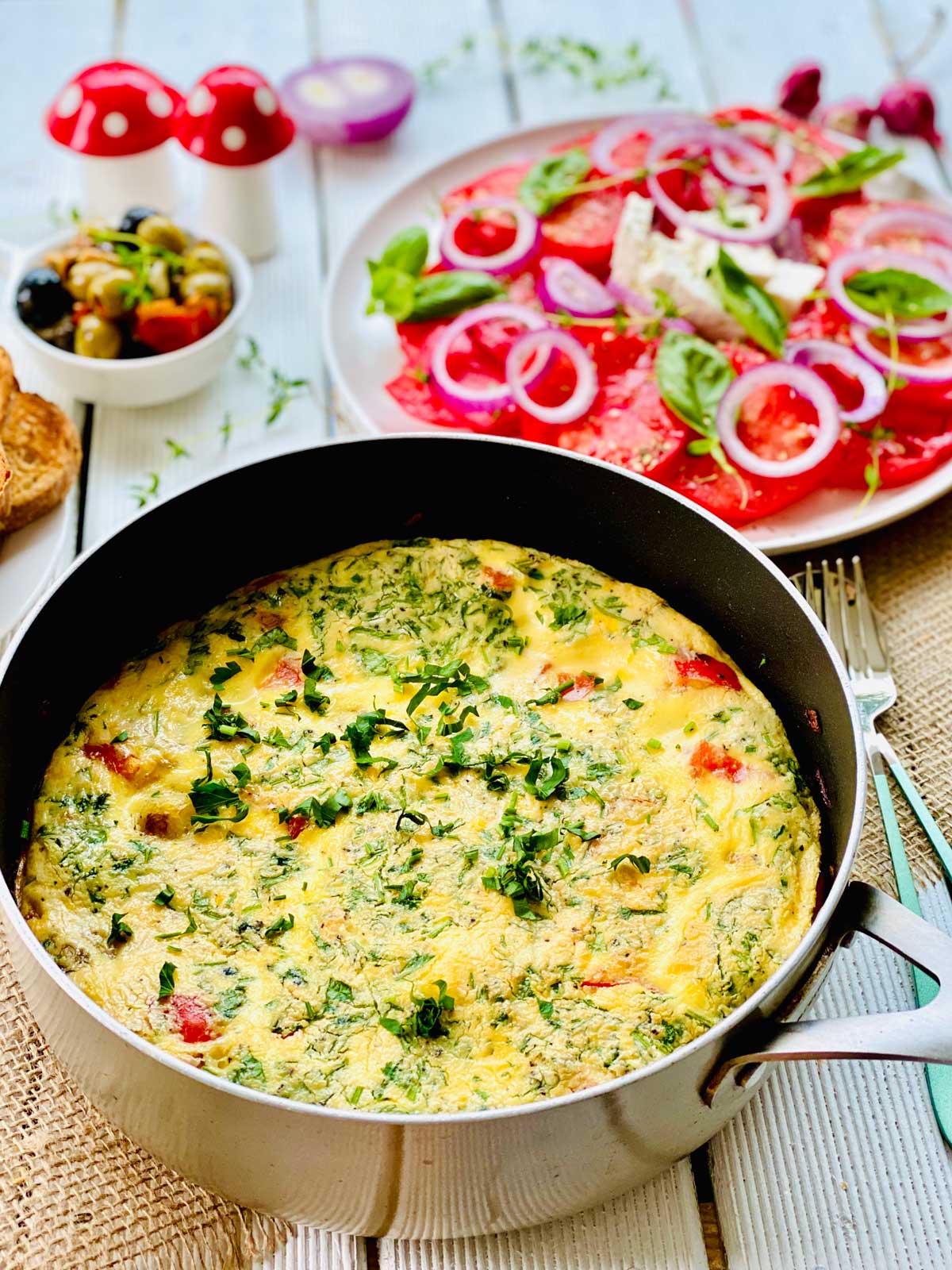 Spanish Omelette In a non-stick pan and a vibrant tomato slice salad topped with red onion rings above.