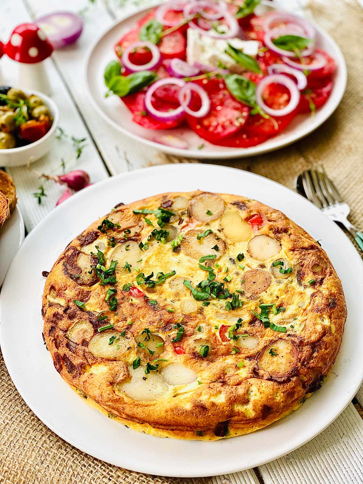 Spanish Omelette on a white plate topped with fresh herbs.