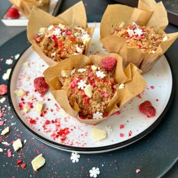 Three raspberry and white chocolate muffins on a white plate.