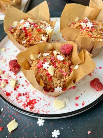 Three raspberry and white chocolate muffins on a white plate.