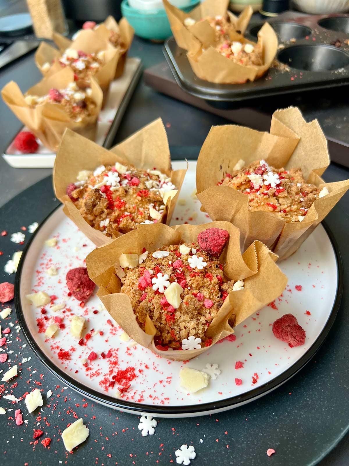 Three raspberry and white chocolate muffins sprinkled with dried raspberries and white chocolate on a white plate.