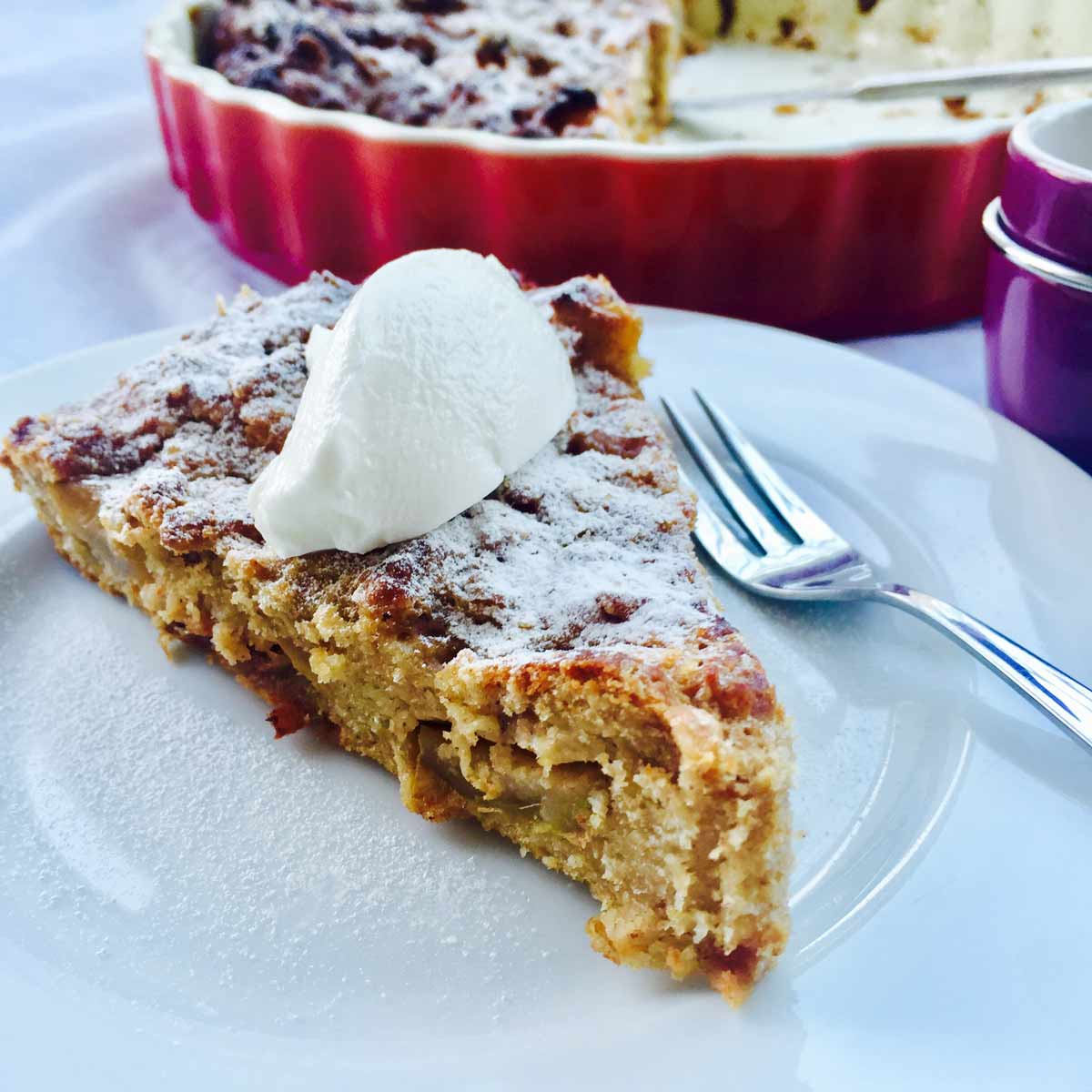 A delicious slice of apple baked oats, topped with a dollop of yogurt on a white plate an d a fork on a side.