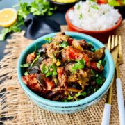 Aubergine curry in a green ceramic serving pot.