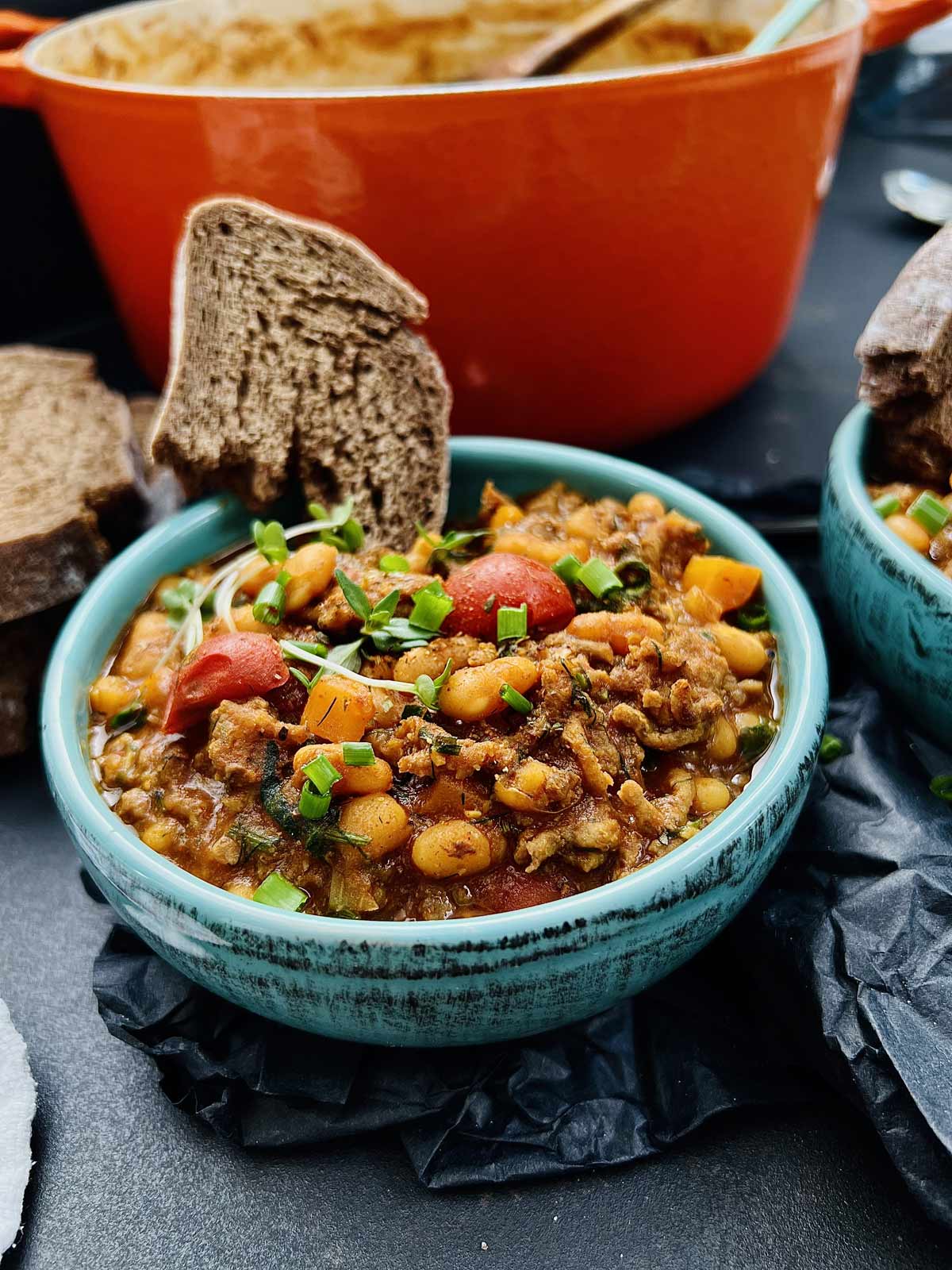 Baked beans recipe with ground beef served in a green serving bowl with a slice of bread tucked in.