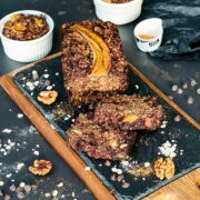 Banana bread with two slices close to the loaf and a few walnuts and barley flakes scattered around.