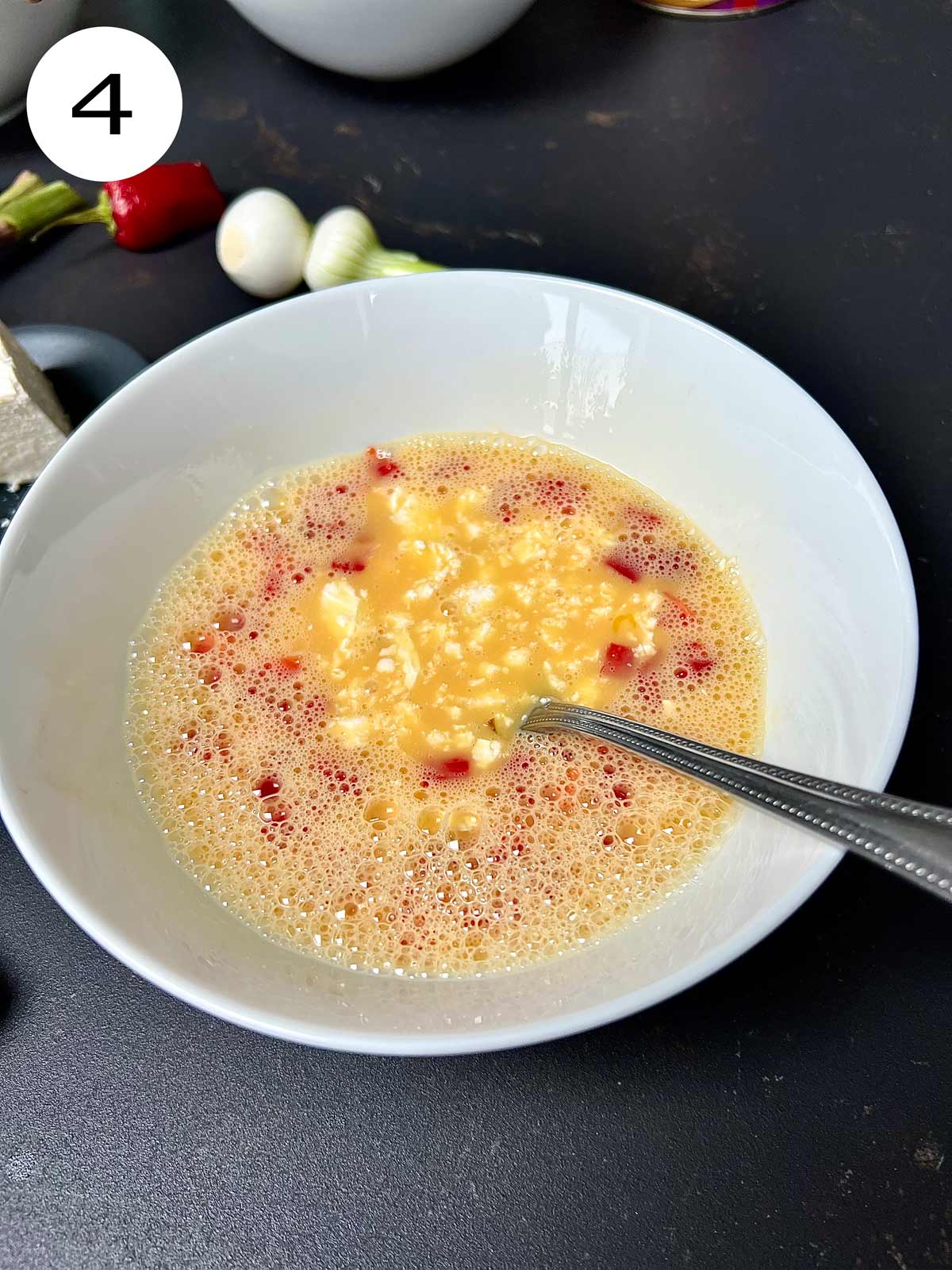 Beaten eggs with some cheese and finely chopped pepper in a white bowl with a metalic fork in.