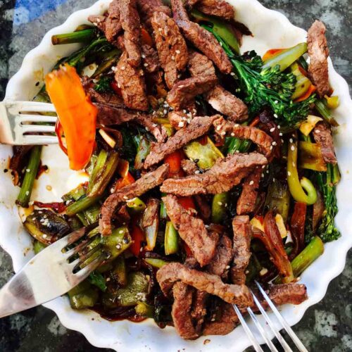 Beef hoisin stir fry with tenderstem broccoli, carrot and green pepper on a white plate