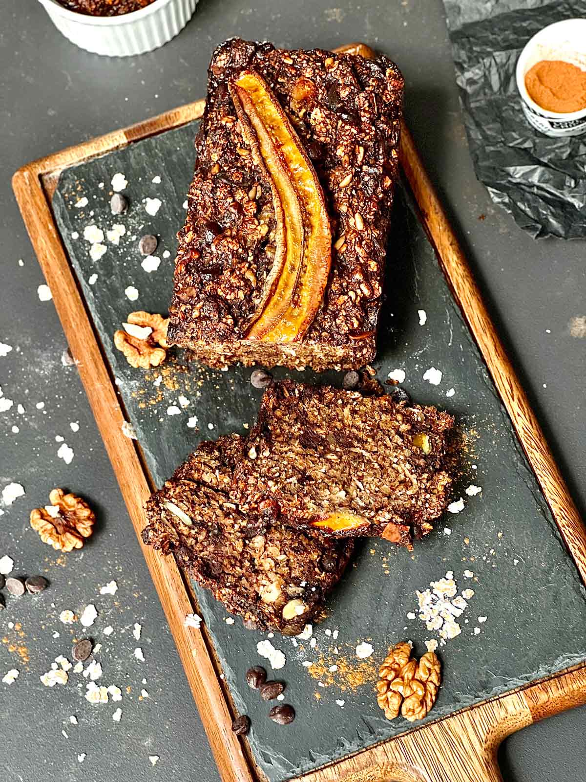 Birdseye view of sliced banana bread with two slices close to the loaf and a few walnuts and barley flakes scattered around.