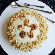 Carrot cake with walnuts on white plate, decorated with crashed walnuts and walnut halves birdseye.